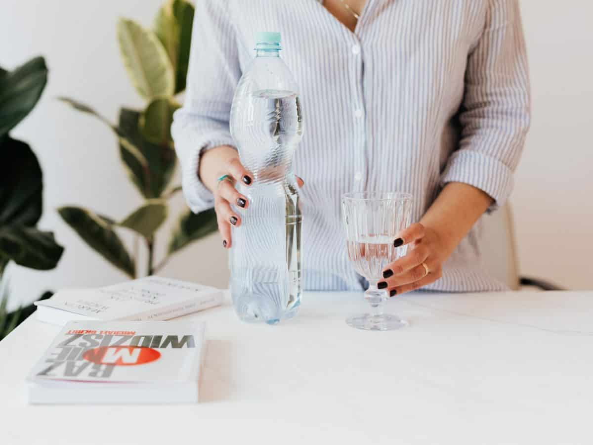 woman in button down shirt with bottled water and water in glass
