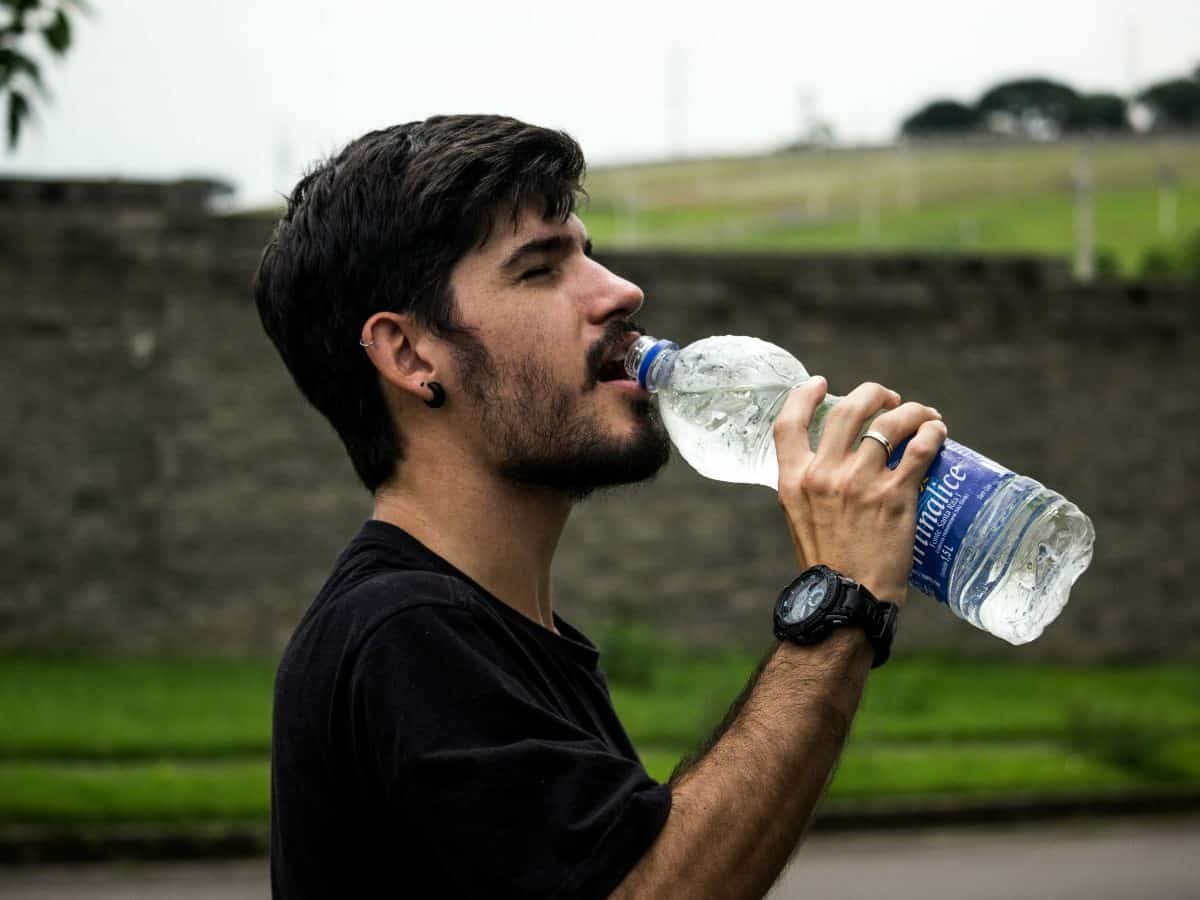man looking right and drinking out of large water bottle
