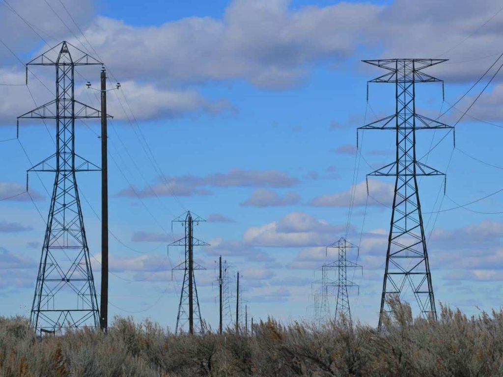 Powerlines standing in a field beneath a light blue sky with clouds.