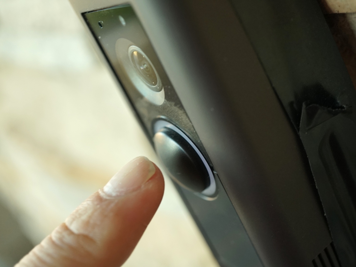 a finger pressing a ring doorbell outside of a home