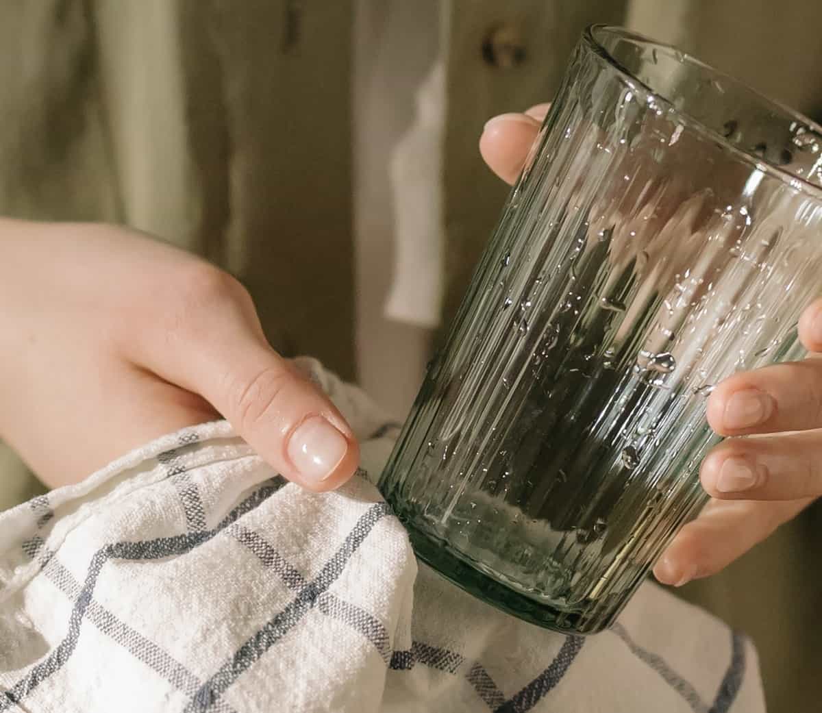 A woman is holding a glass on top of a towel that's wet with water droplets.