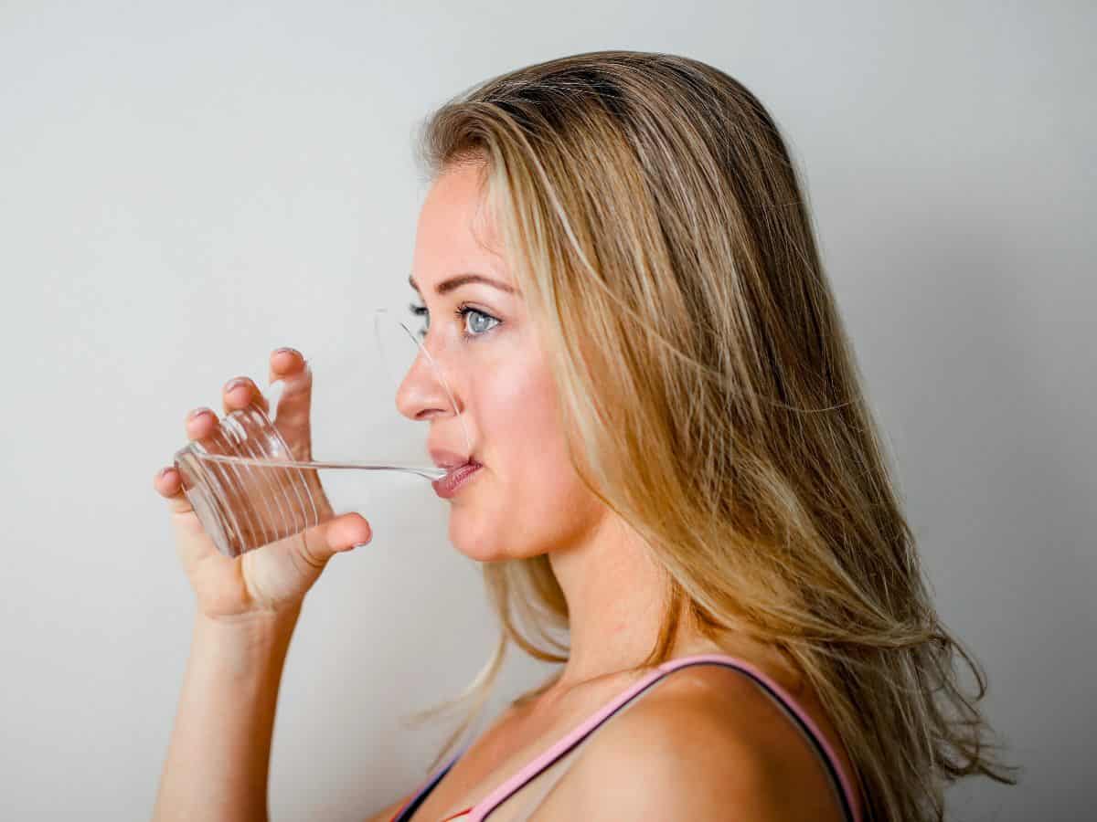 blonde woman looking left and drinking water from glass