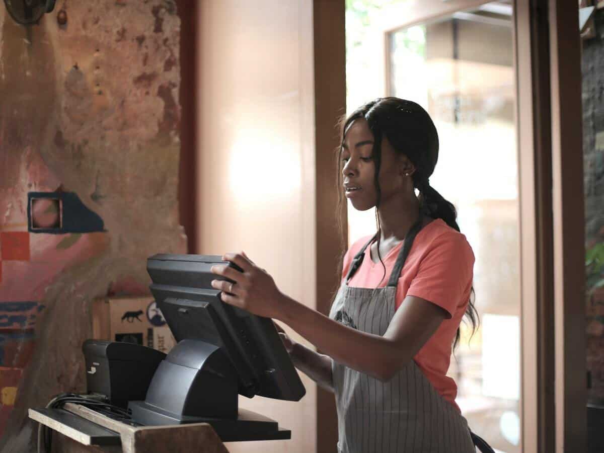 A young female cashier standing in front of a computer inside of a shop.