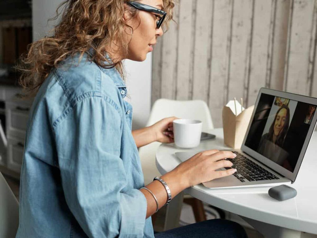 A woman with curly light brown hair is video chatting with a woman on her laptop.