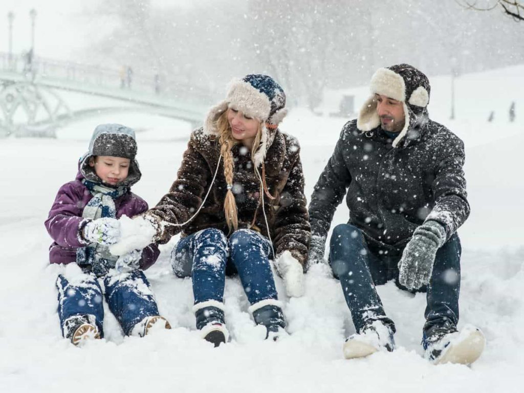 family of three sitting in the snow together