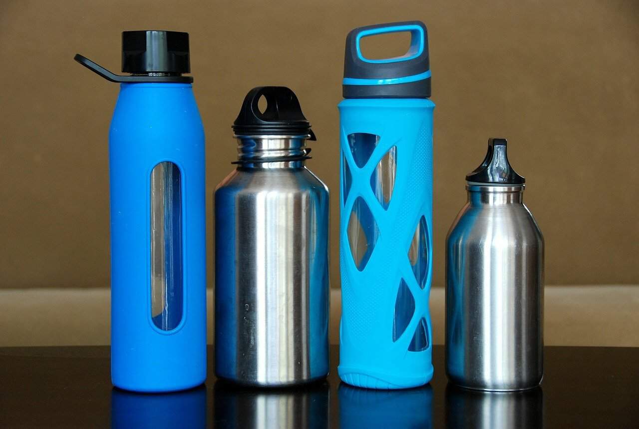 A row of four filtered water bottles made of different materials sit on a dark surface.