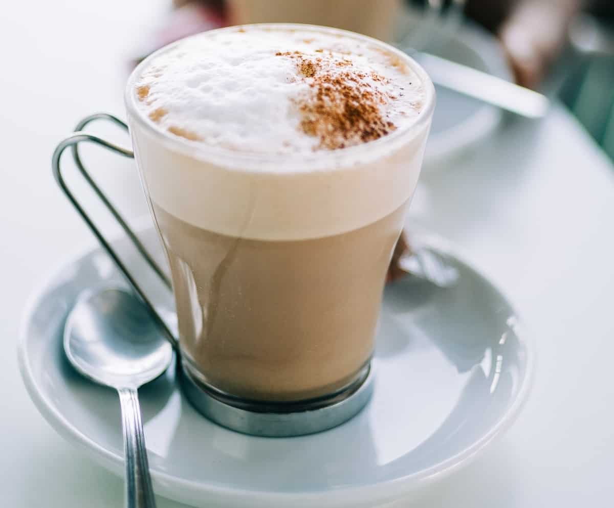 A glass mug sitting on a saucer is filled with a hot beverage topped with layers of froth.