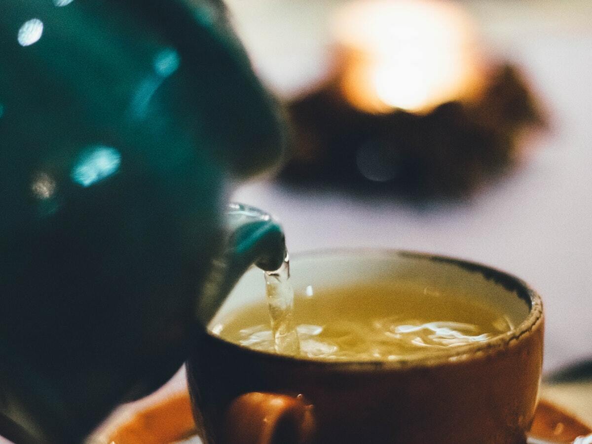 A green teapot pouring green tea into a brown mug.