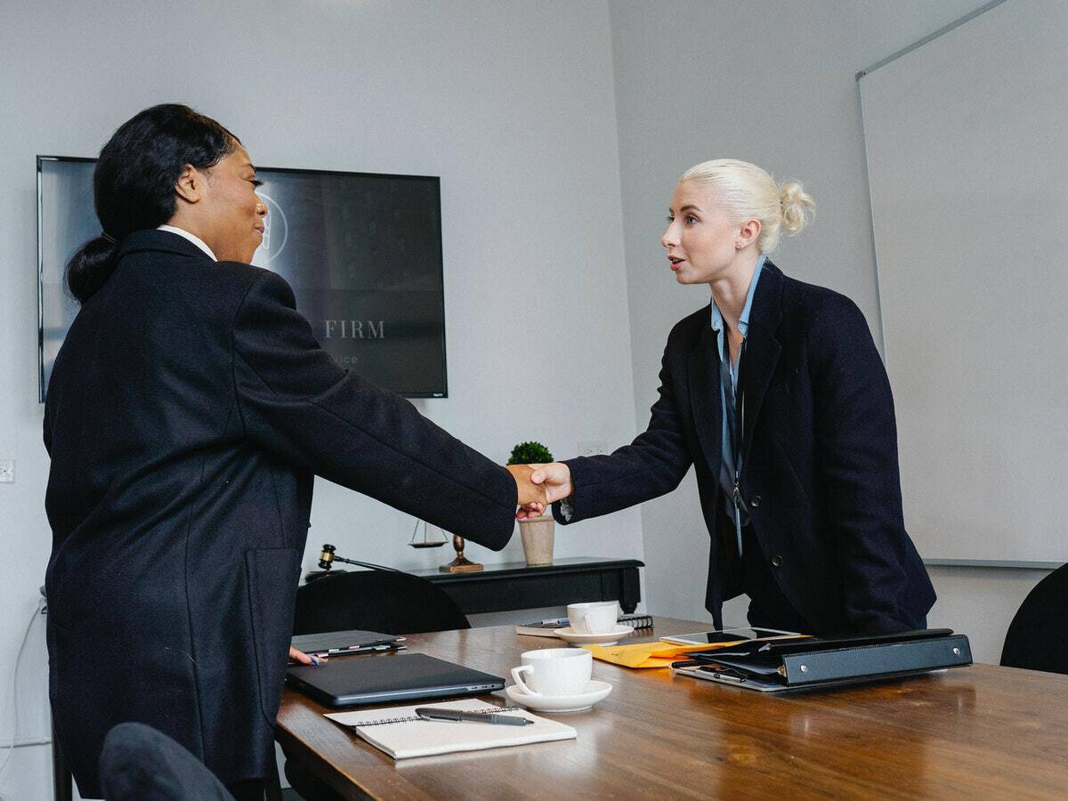 A woman shakes the hand of a female insurance provider inside of an office setting.