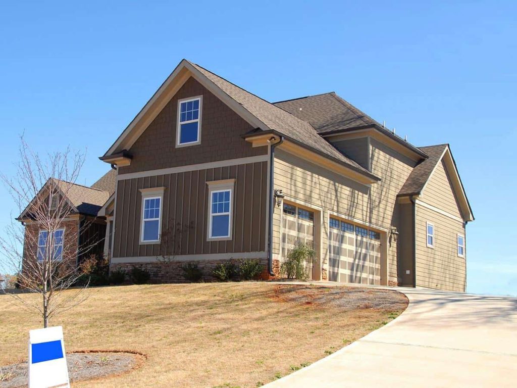 A brown suburban home with a real estate sign on the front lawn.