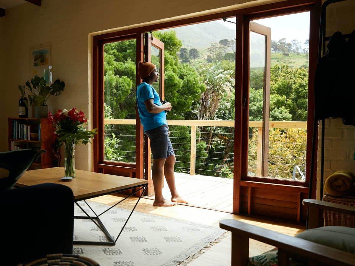 A young man stares out his patio that overlooks trees.