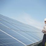 professional man in hardhat with clipboard overlooking solar panels