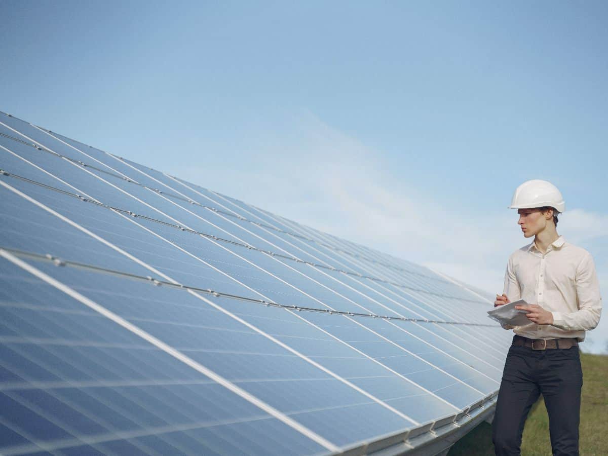 professional man in hardhat with clipboard overlooking solar panels