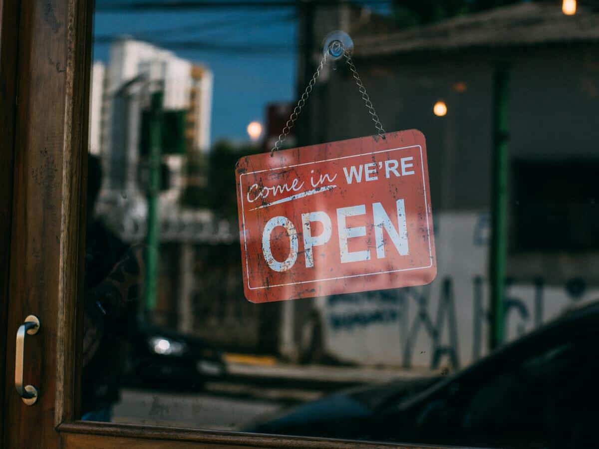 A red sign reading "Come in, we're open" is on the glass door of a business.