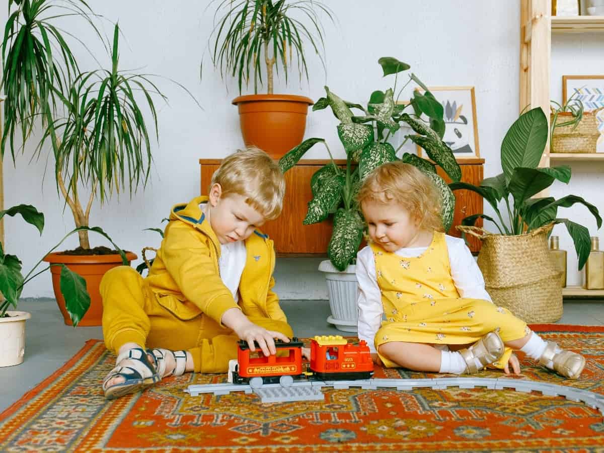 two children playing with a train in front of home plants