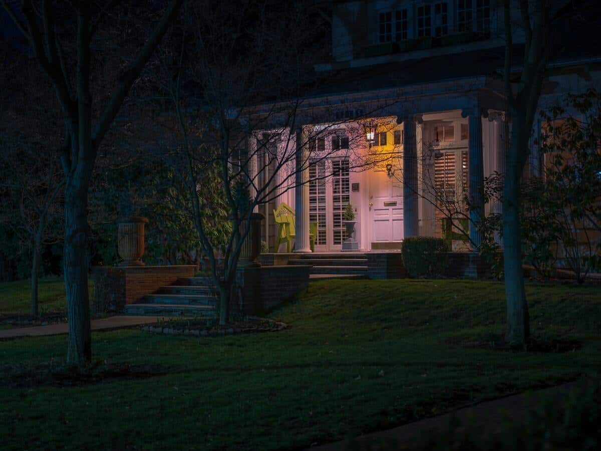 The front of a home surrounded by trees with a security light glowing by the front door.