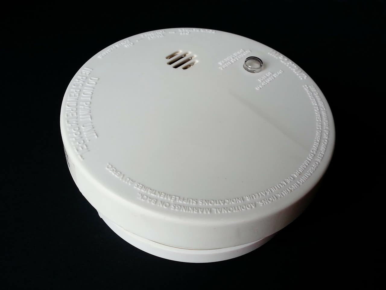 A white smoke detector sitting against a black background.