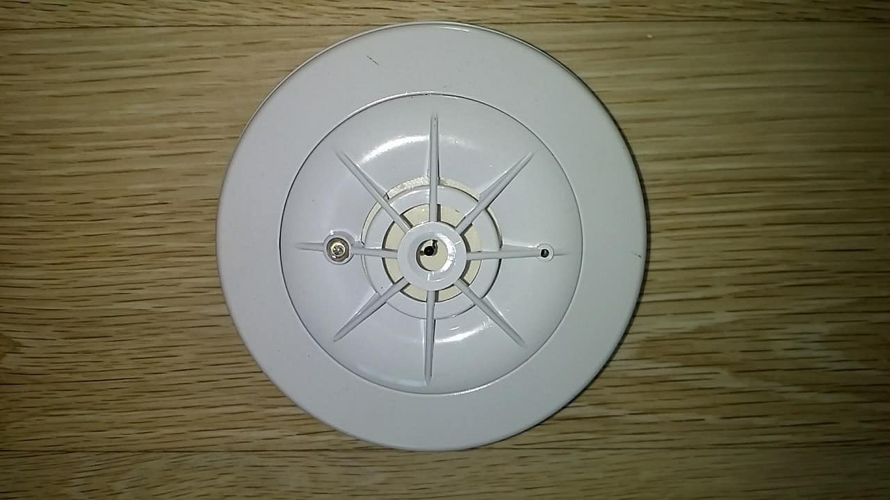 A white smoke detector sitting on top of a brown wooden surface.