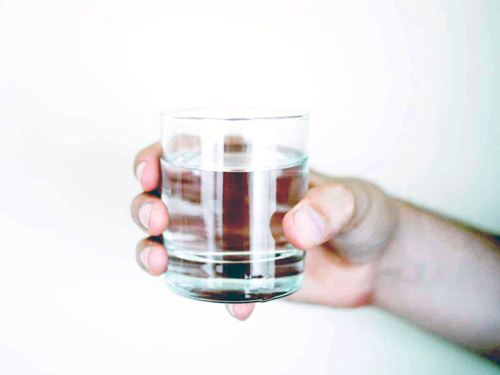 a hand holding a small glass of water against a bare wall