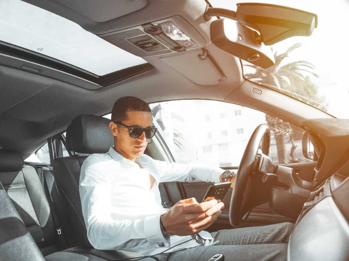 man holding cell phone while driving in car