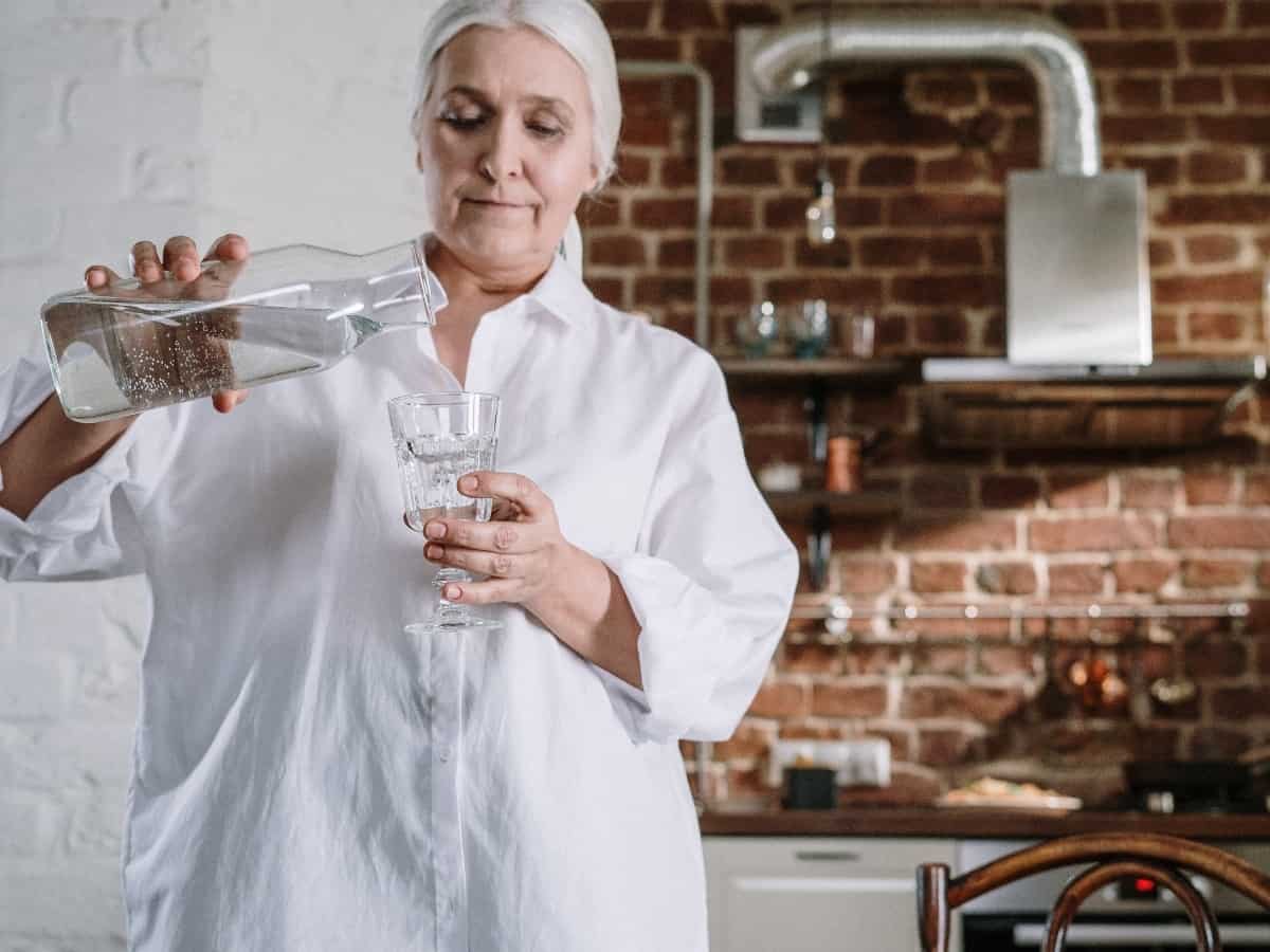 older woman pouring tap water into clear glass for consumption