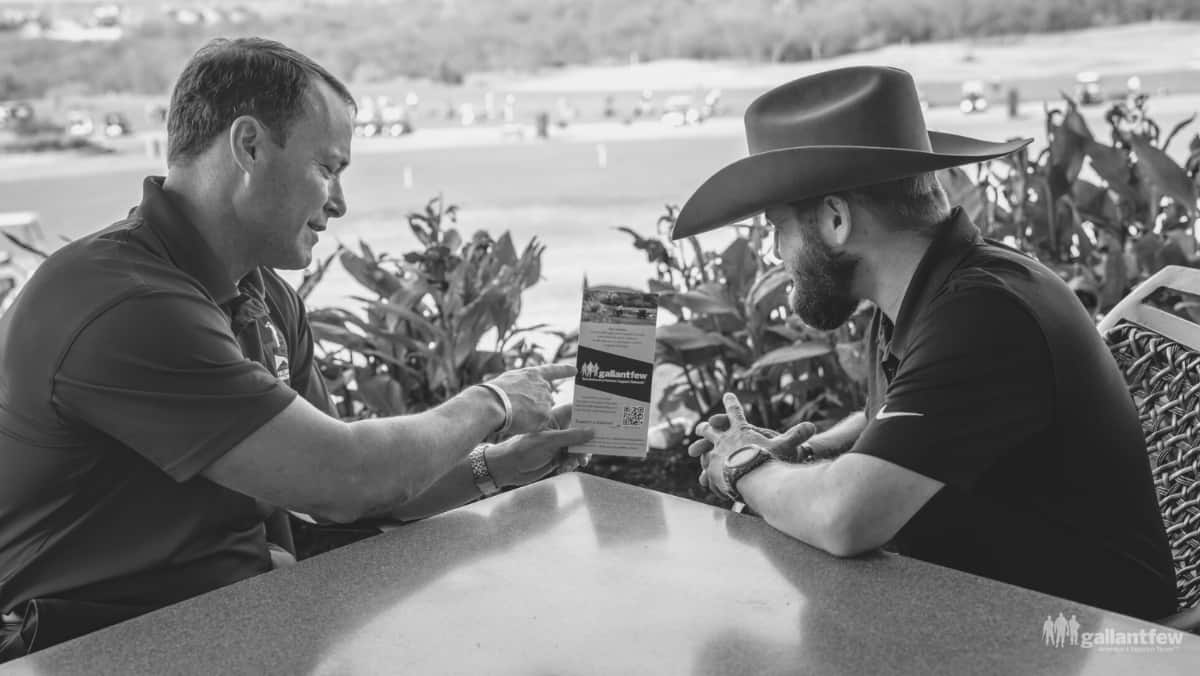 Two men sitting at a table are looking at a GallantFew brochure.