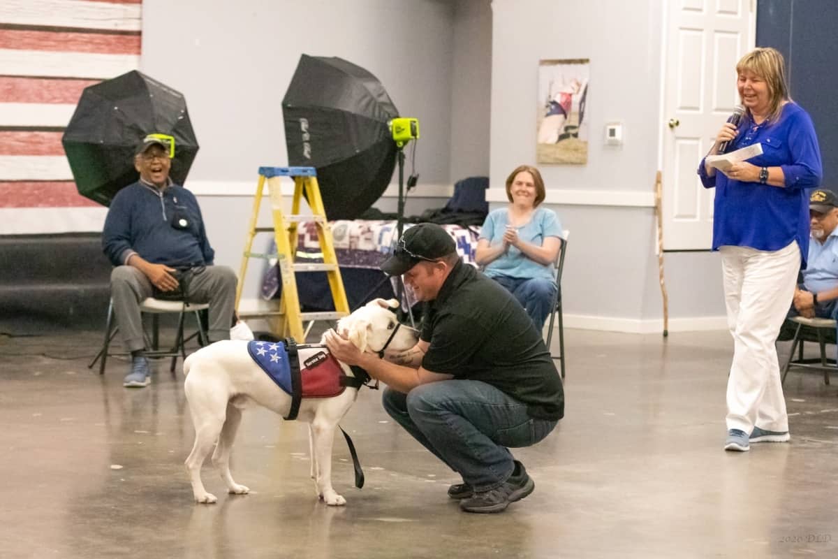 A Veteran is kneeling down to hold his service dog close to him.