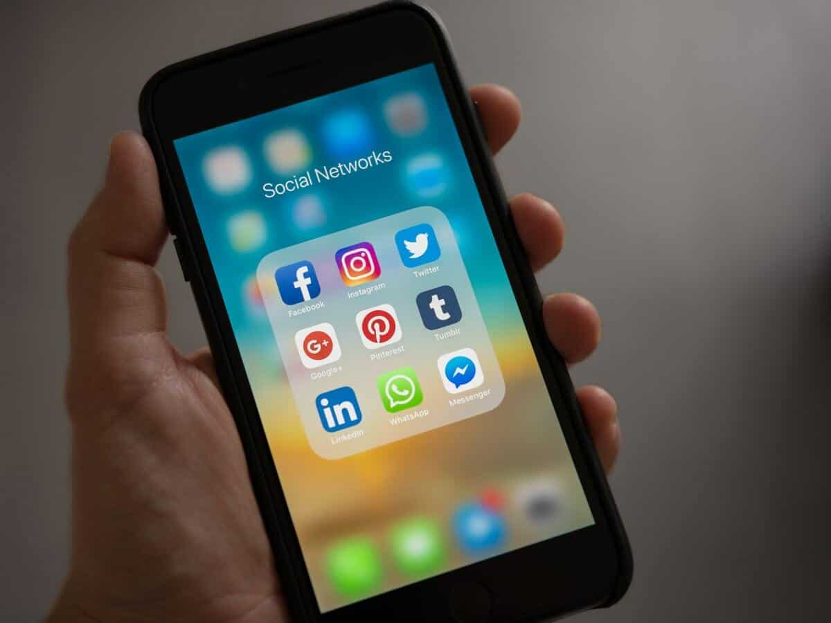 Closeup of a hand holding a black smartphone that’s opened to a social media folder displaying different social media applications.