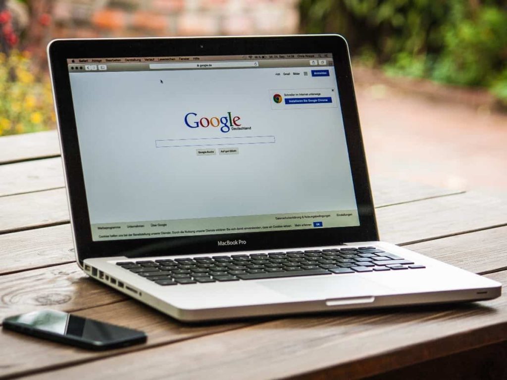 a laptop with google on the homepage and a cell phone on the table