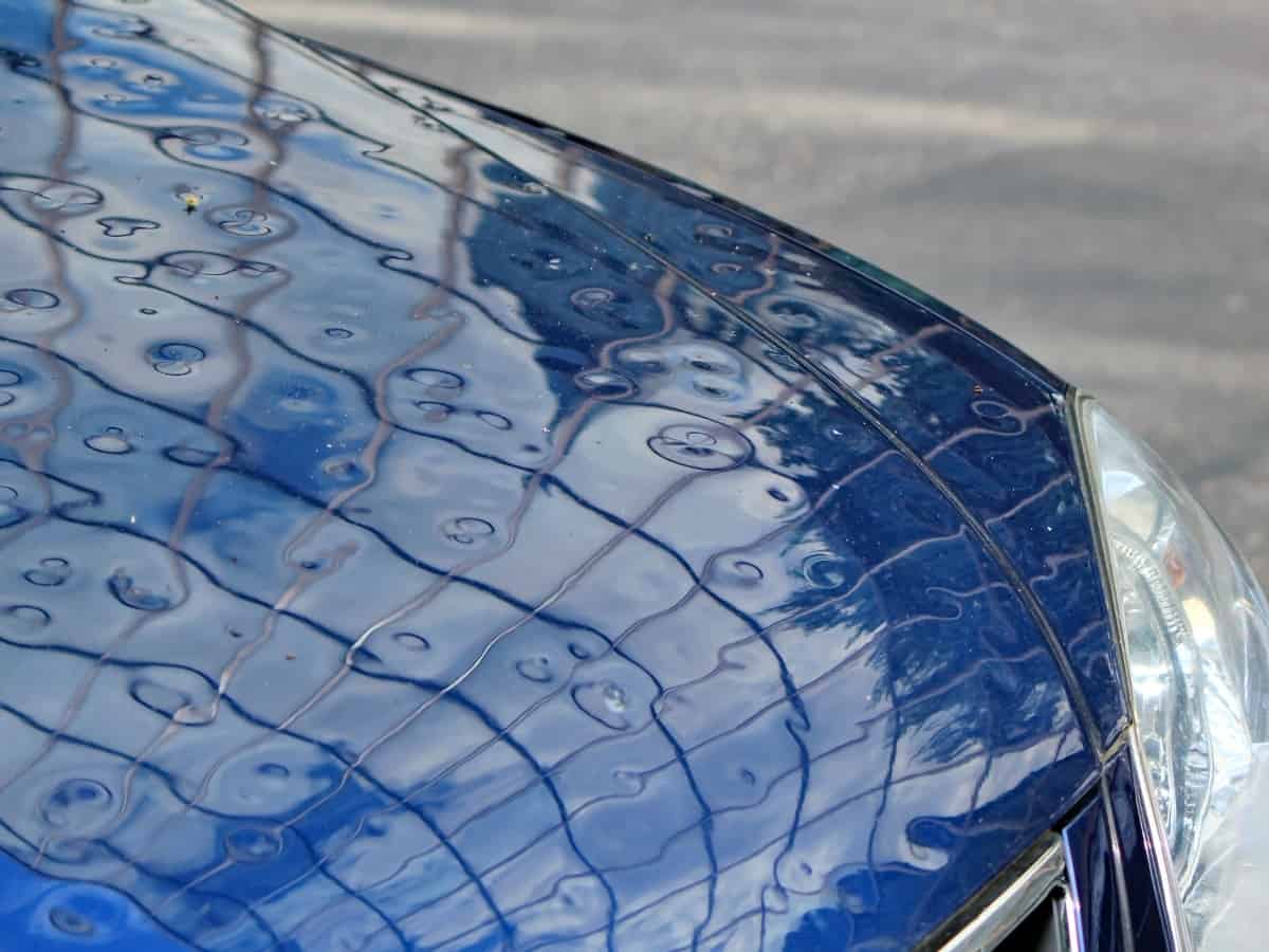 close up of a blue car with hail damage on the hood