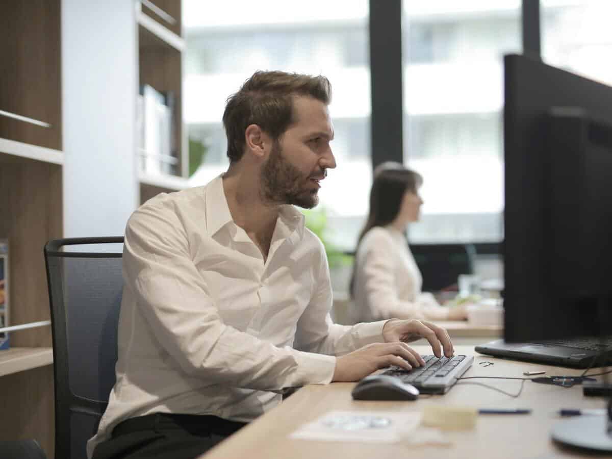 A young man is working on a computer in an office setting.