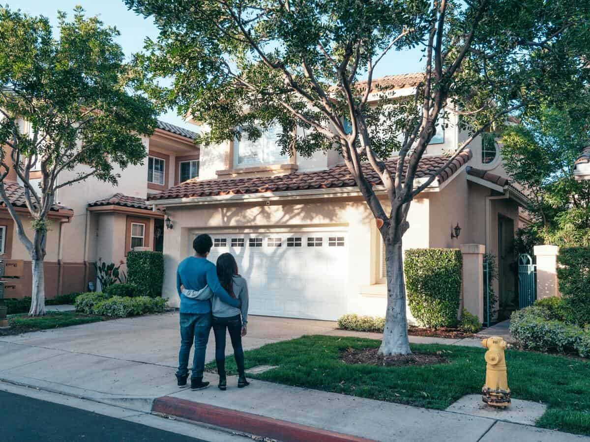 A couple stands outside in front of their home, looking up at the property.