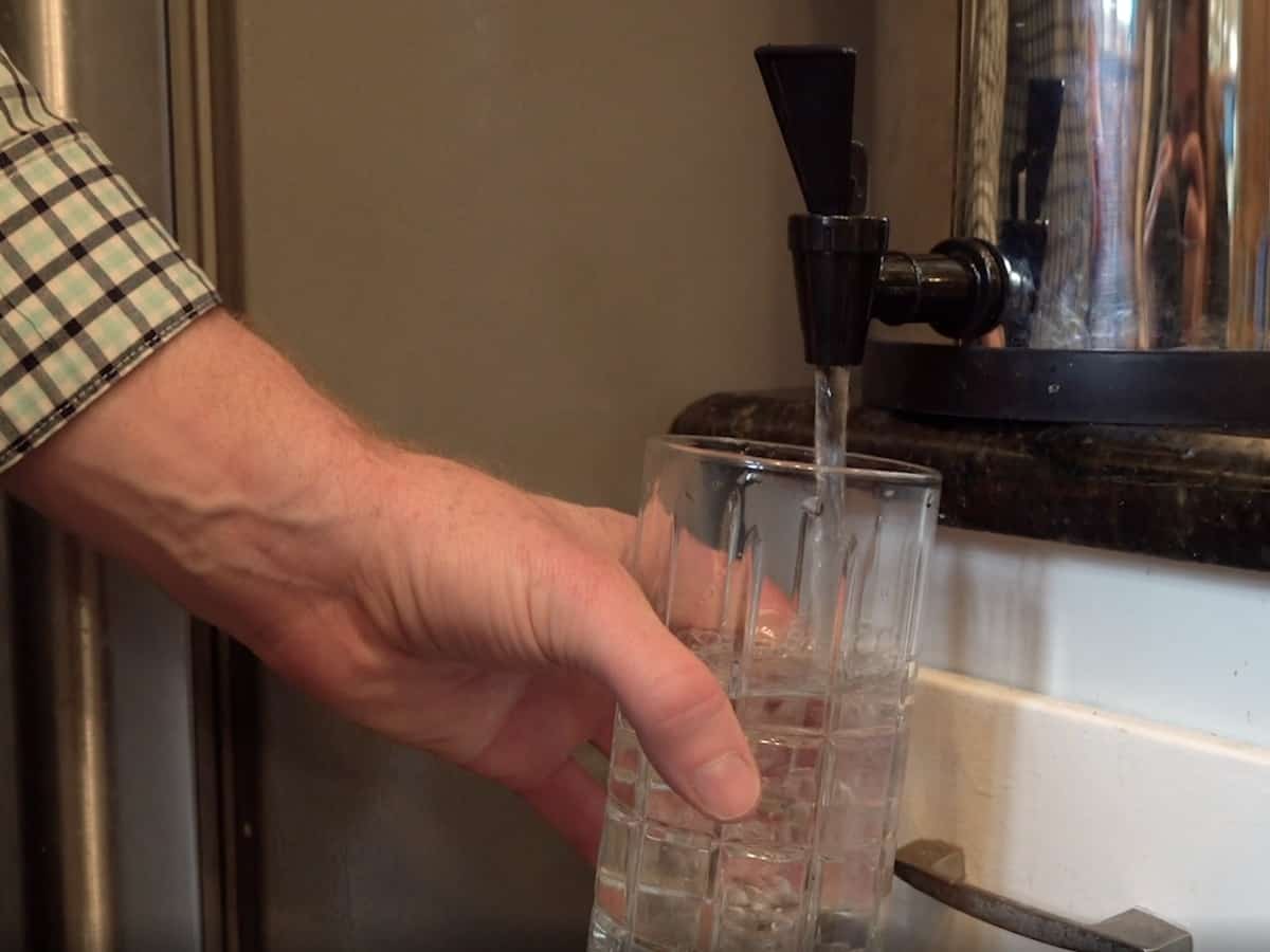 a man filling up a glass of water after using a home water filtration system