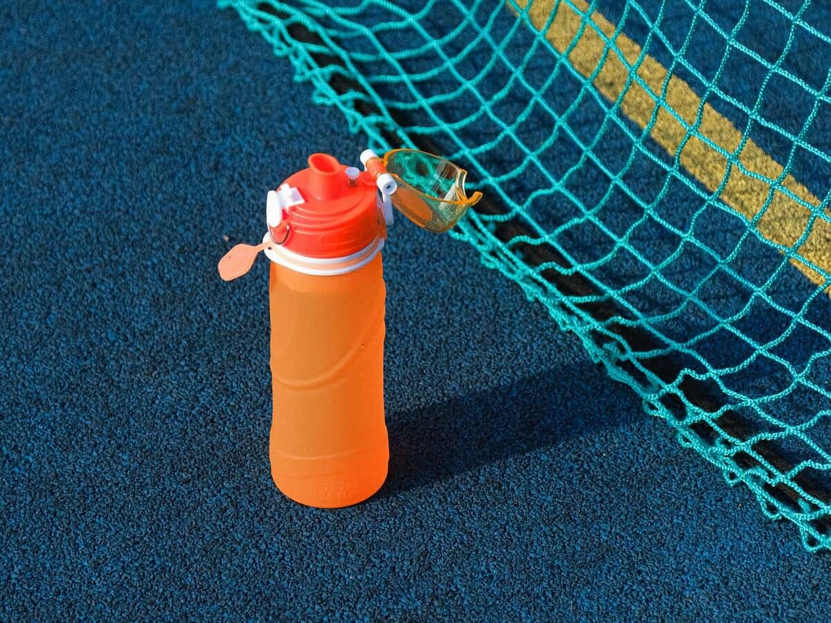 A closeup of an orange reusable water bottle that's on a dark blue tennis court.