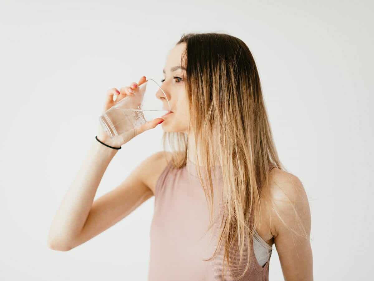 A girl in a pink t-shirt is drinking water while looking to the left.