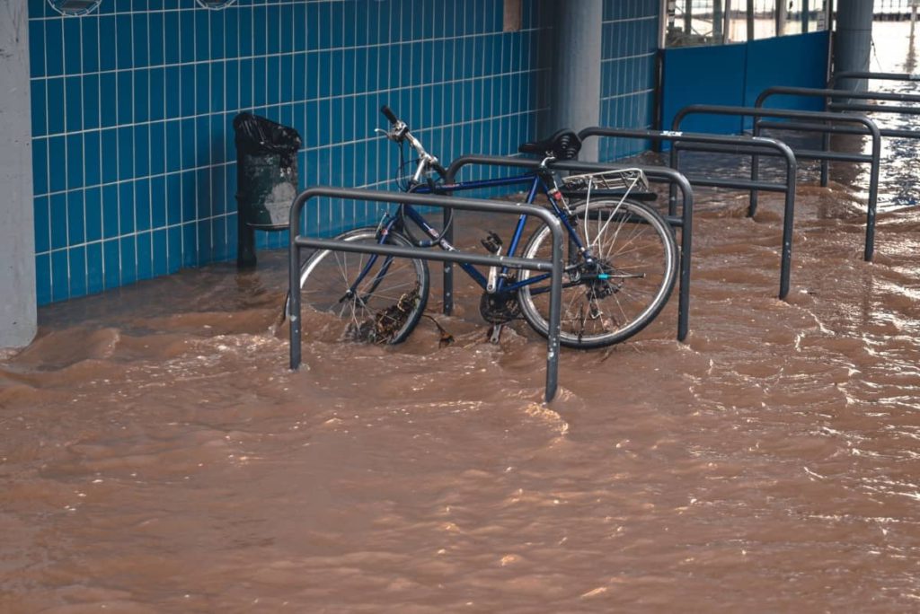 A bike hooked up to a rack is surrounded by floodwater.