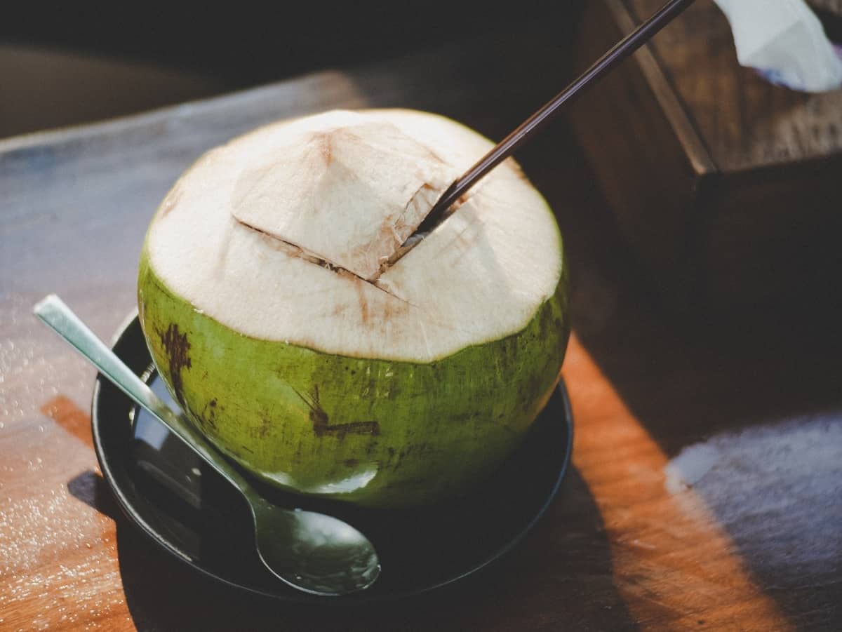 a green coconut with a straw to drink coconut water as a post workout drink for hydration