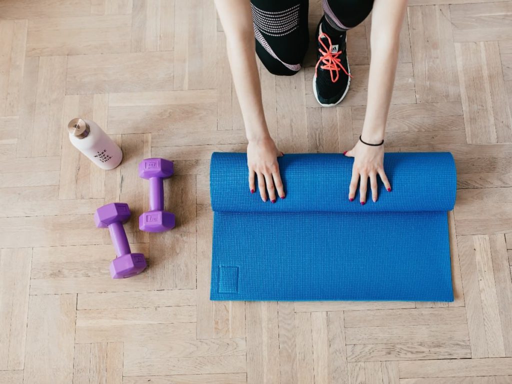 a woman rolling up a blue yoga mat with purple weights and a water bottle
