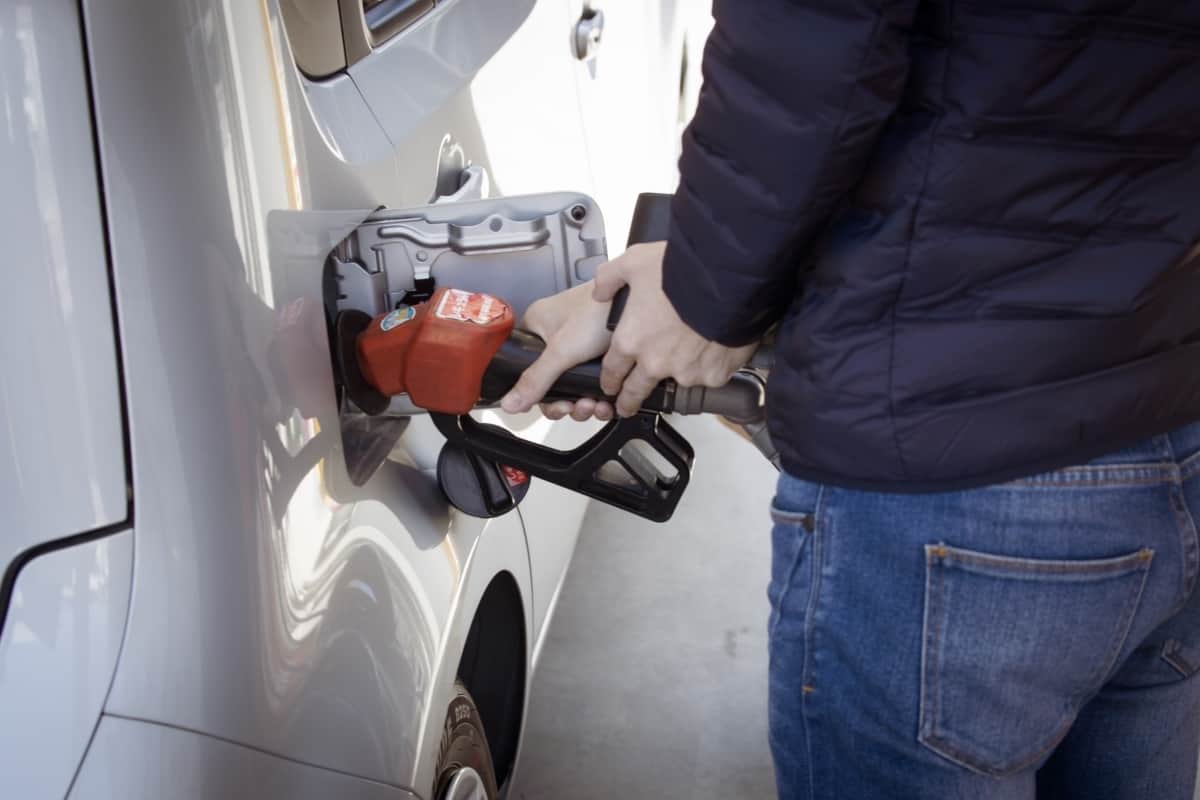 A man is filling up his car with gas from a red pump.