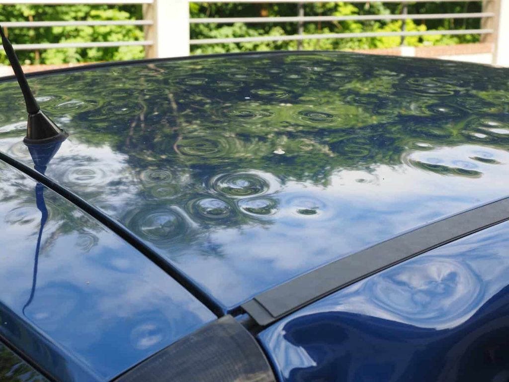 Close up of a blue car with dents from hail damage.