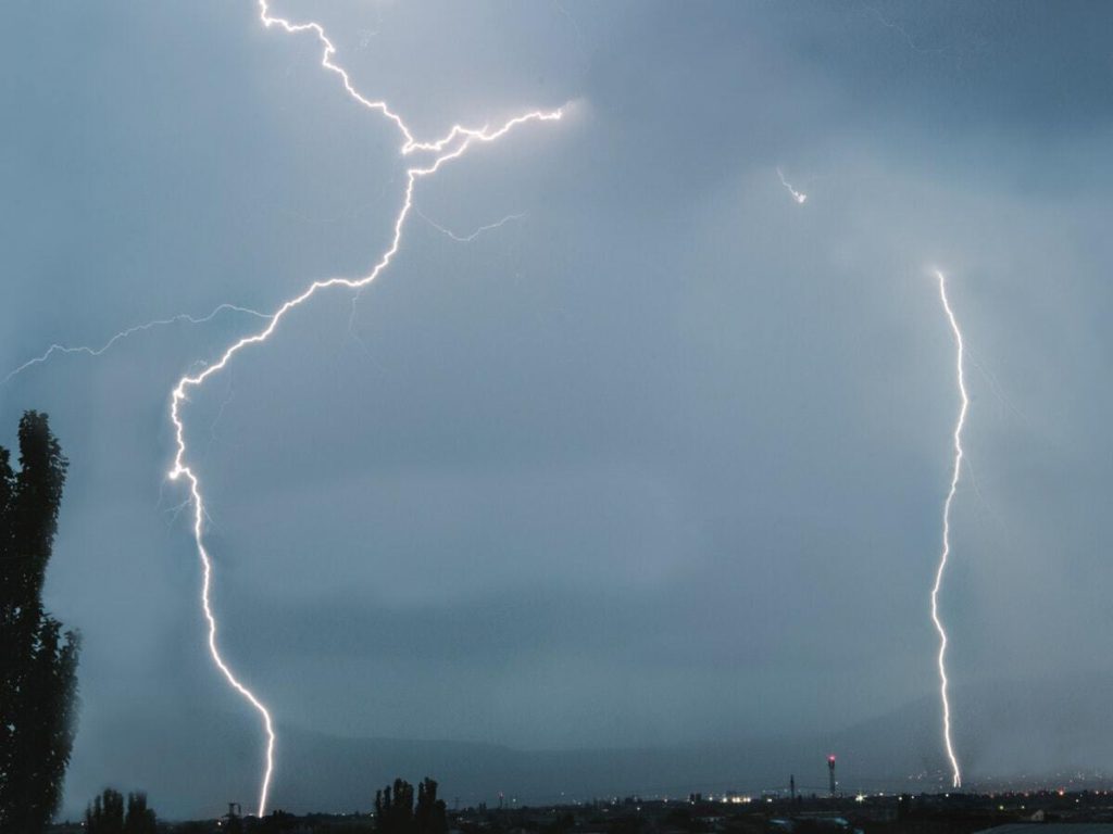 Two lightning bolts striking down onto the ground from a grey sky.