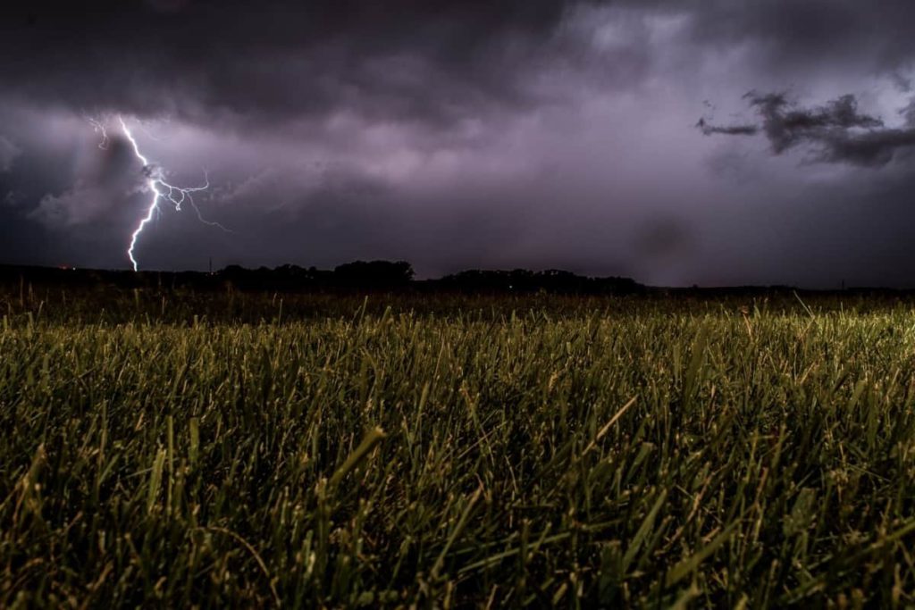 Lightning striking down near a field of grass.