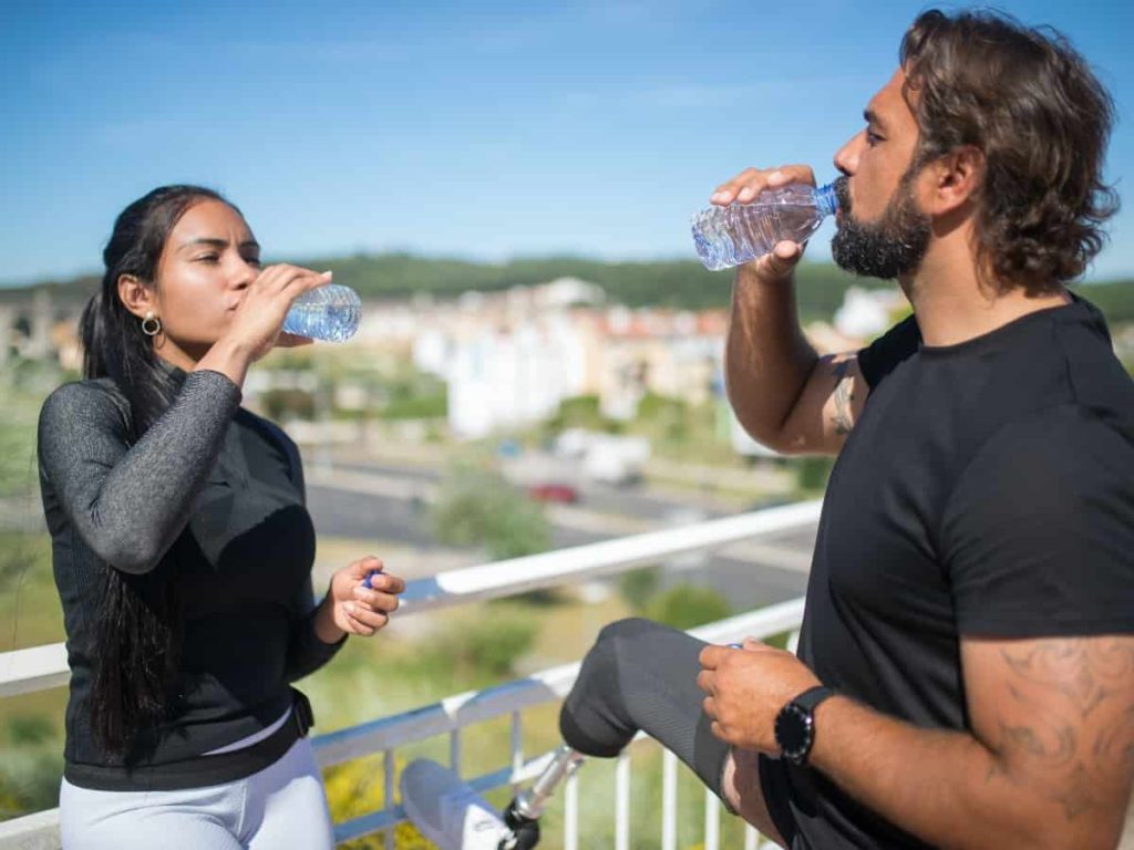 man and woman standing outside drinking water to stay hydrated during the summer