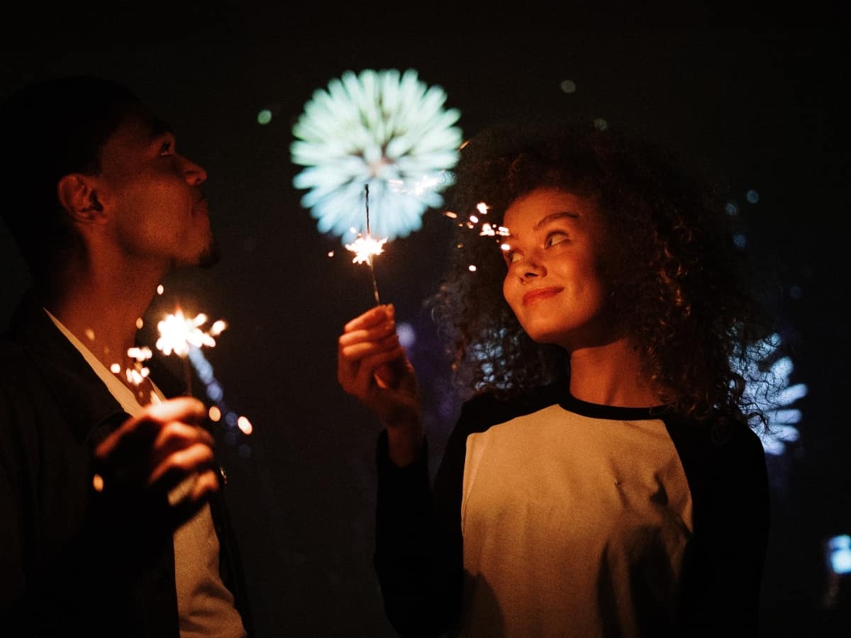 boy and girl hold sparklers with fireworks in the background