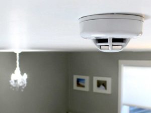 A white smoke detector is hanging on a ceiling inside of a home.