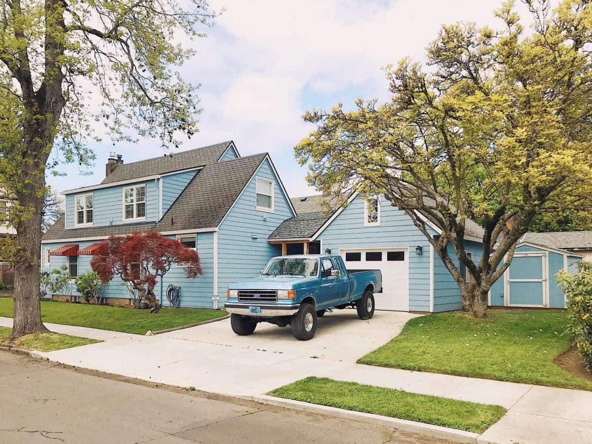 A blue house has a blue pickup truck parked on the driveway.