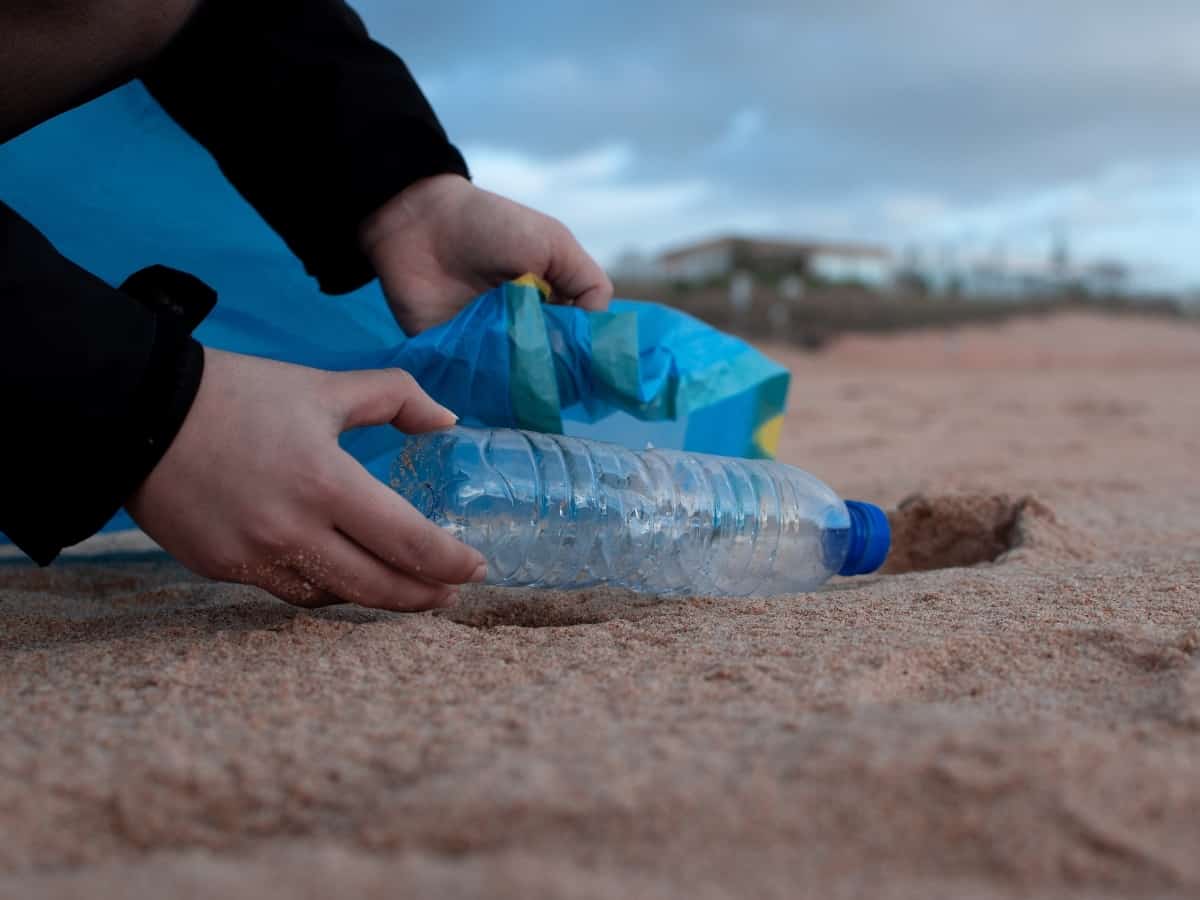picking up a plastic bottle from the beach to reduce plastic waste and reduce environmental impact