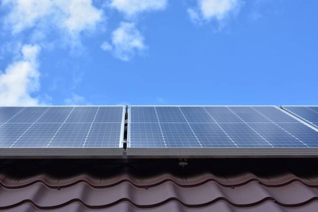 Solar panels on a brown roof looking up at a blue sky with a few scattered clouds.