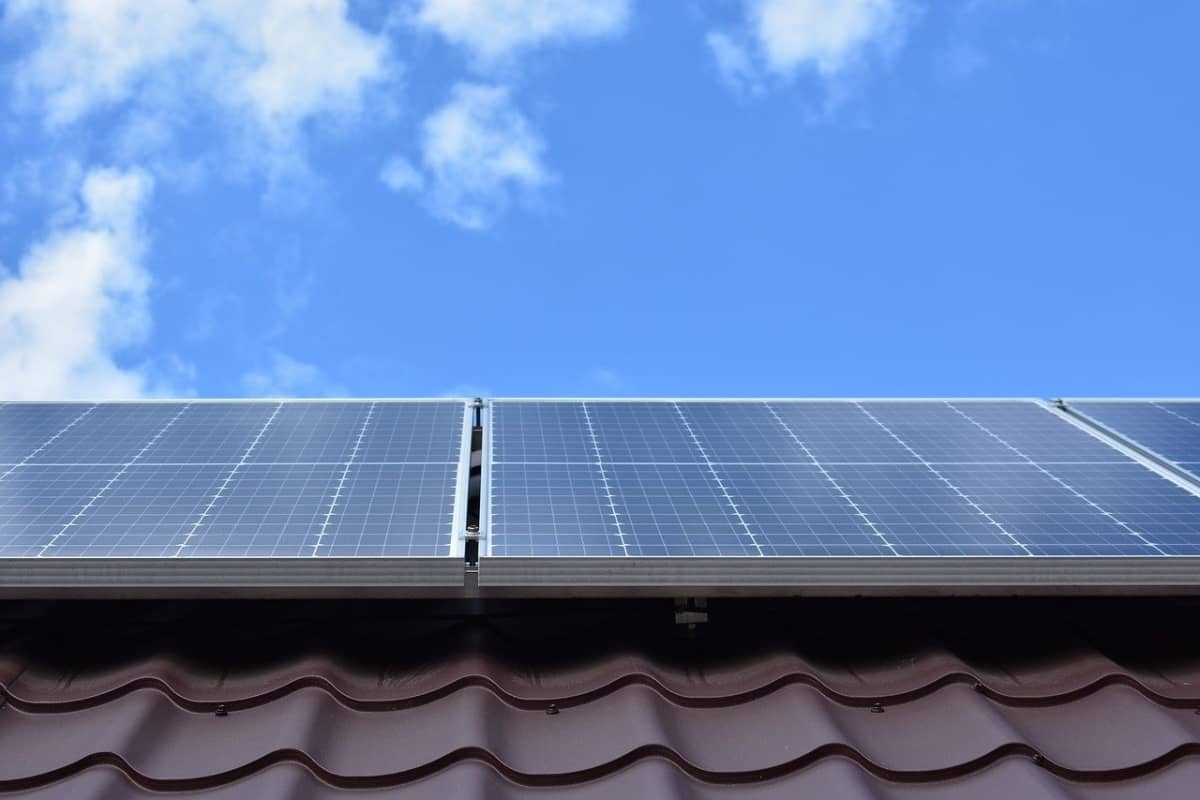 Solar panels on a brown roof looking up at a blue sky with a few scattered clouds.