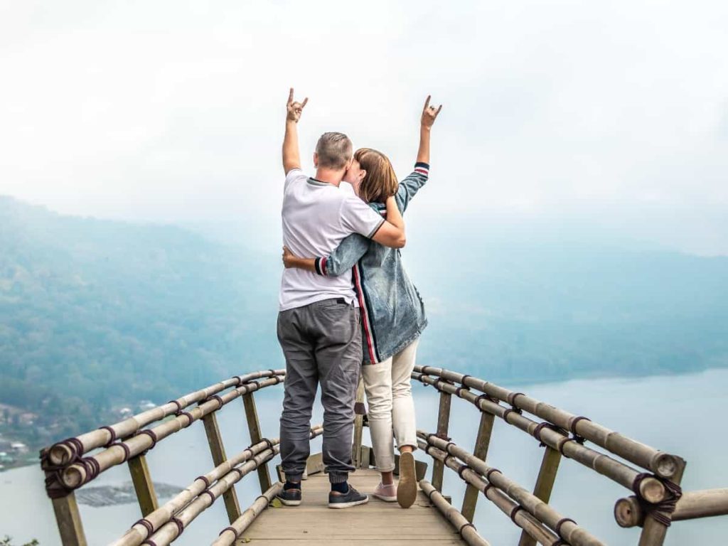 a couple standing on a bridge with their hands up enjoying life